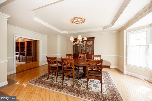 dining space with a tray ceiling, an inviting chandelier, light wood-style flooring, and ornamental molding