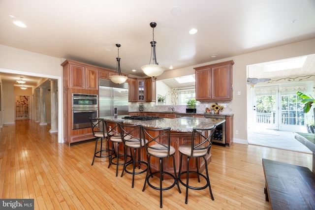 kitchen with a sink, brown cabinetry, a skylight, light wood-type flooring, and backsplash