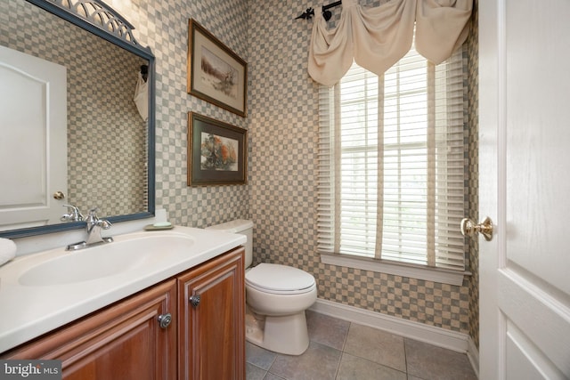 bathroom featuring toilet, vanity, tile patterned floors, baseboards, and wallpapered walls