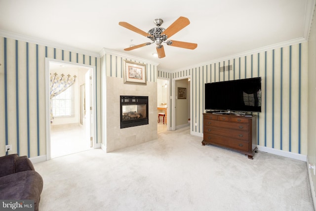 carpeted living area featuring ceiling fan, ornamental molding, a tiled fireplace, and wallpapered walls