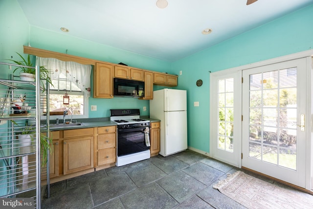 kitchen featuring freestanding refrigerator, stone tile flooring, gas range, baseboards, and black microwave