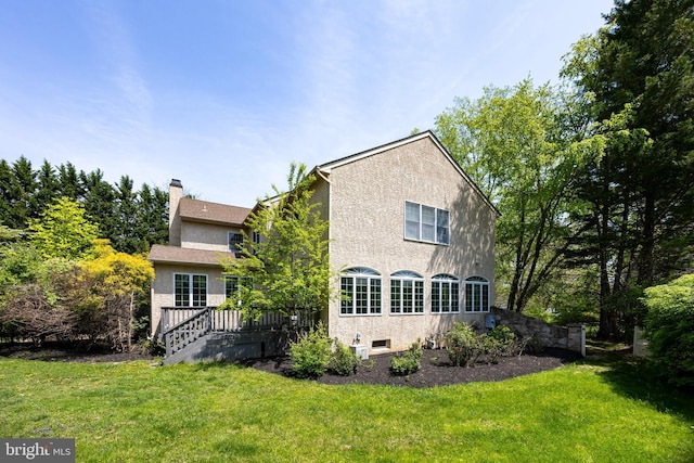 back of house with a lawn, a chimney, a wooden deck, and stucco siding