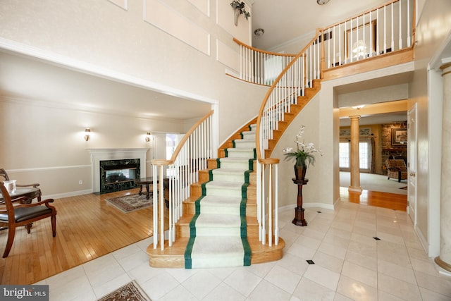 stairs with tile patterned floors, a high end fireplace, decorative columns, and a towering ceiling