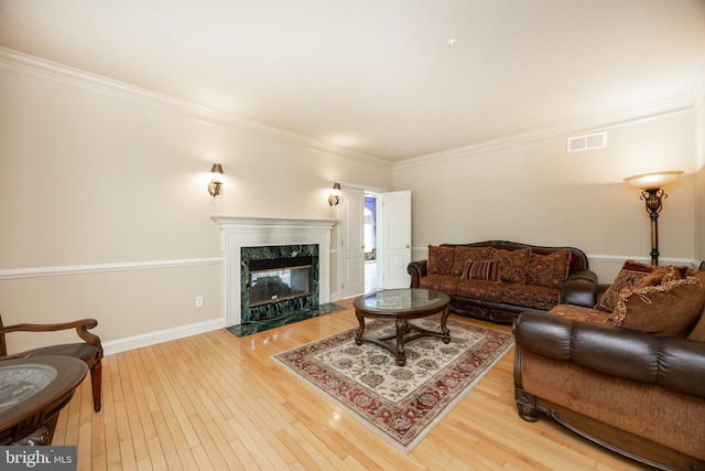 living area with a premium fireplace, baseboards, ornamental molding, visible vents, and hardwood / wood-style flooring