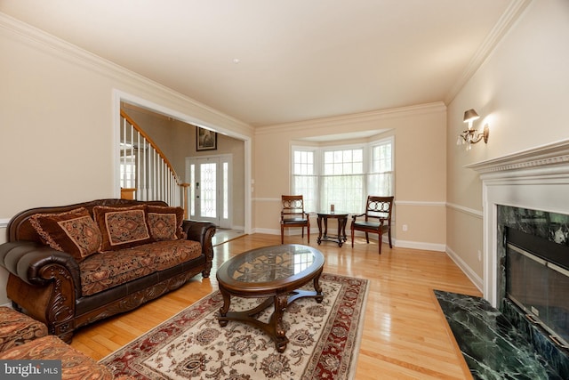 living room featuring a premium fireplace, crown molding, stairway, baseboards, and light wood-style floors