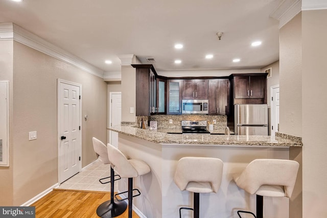 1530 Spring Gate Dr Unit 9208, Mclean, VA 22102 - kitchen featuring stainless steel appliances, decorative backsplash, crown molding, a kitchen bar, and dark brown cabinetry