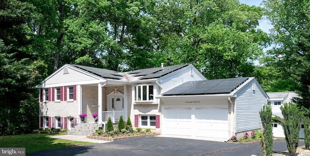 view of front facade with brick siding, driveway, solar panels, and a garage