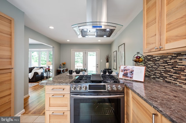 kitchen featuring stainless steel range with gas cooktop, backsplash, dark stone countertops, and island exhaust hood
