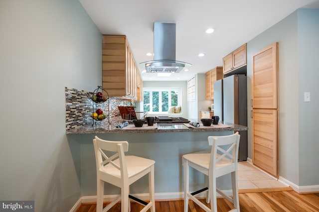 kitchen featuring freestanding refrigerator, recessed lighting, island exhaust hood, a peninsula, and tasteful backsplash