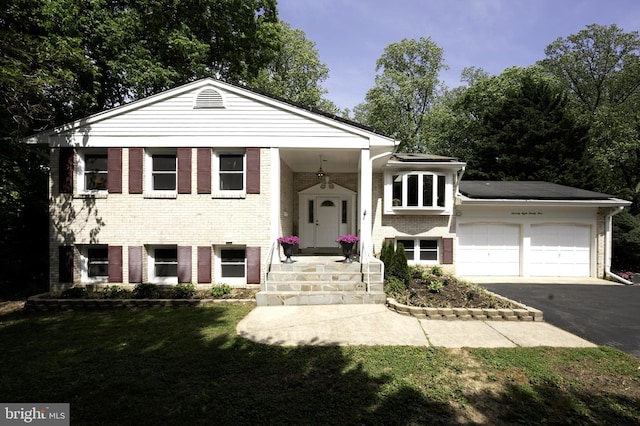 raised ranch featuring a front lawn, brick siding, an attached garage, and aphalt driveway