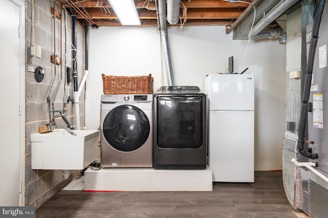 washroom with heating unit, washing machine and dryer, wood finished floors, a sink, and laundry area