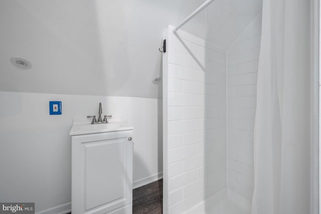 bathroom featuring baseboards, lofted ceiling, a tile shower, and a sink