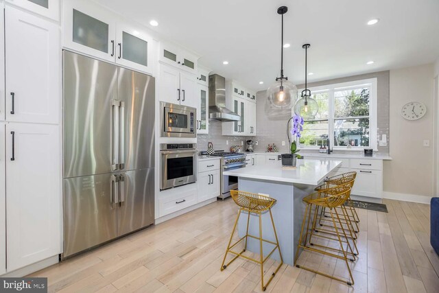 5116 Lawton Dr, Bethesda, MD 20816 - kitchen with premium appliances, wall chimney range hood, decorative backsplash, light wood-style flooring, and a kitchen bar