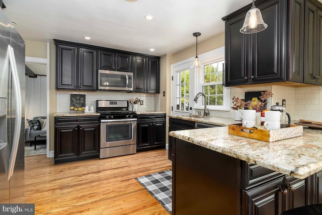 kitchen with decorative light fixtures, appliances with stainless steel finishes, tasteful backsplash, light wood-type flooring, and a sink
