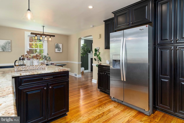 kitchen with stainless steel fridge, light wood-type flooring, light stone counters, arched walkways, and decorative light fixtures