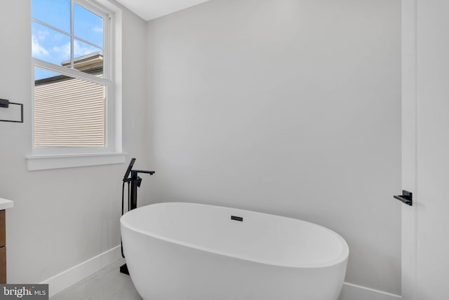 full bath with baseboards, a soaking tub, and vanity