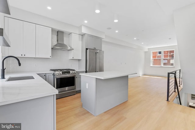 kitchen featuring wall chimney range hood, a sink, stainless steel appliances, light wood-type flooring, and a kitchen island