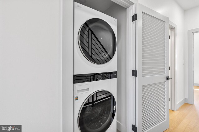 clothes washing area with baseboards, laundry area, stacked washer / dryer, and wood finished floors