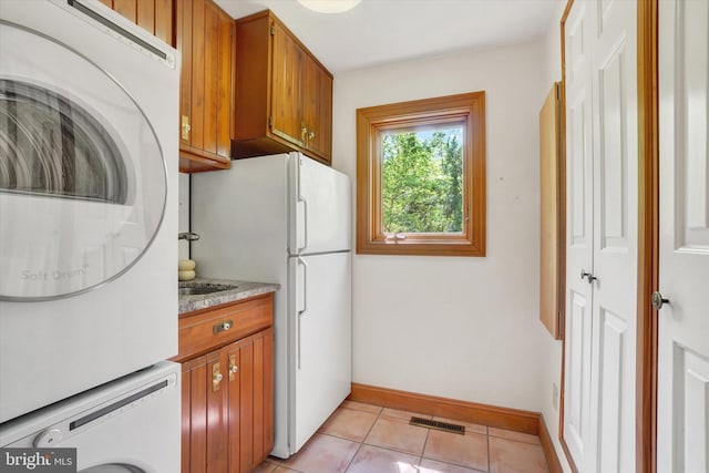 kitchen with freestanding refrigerator, light tile patterned floors, brown cabinetry, and stacked washer / drying machine