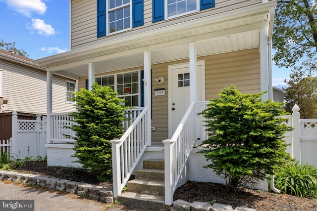 view of exterior entry featuring covered porch and fence