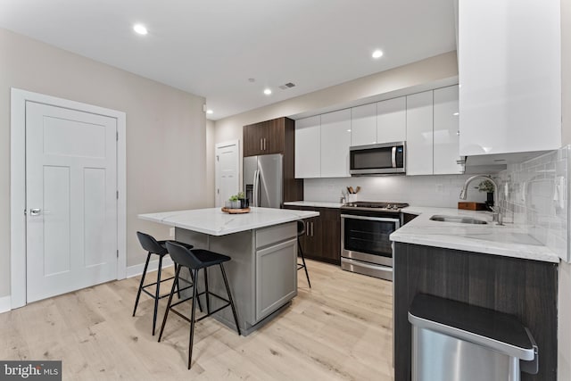 818 Kennedy St NW Unit 9, Washington, DC 20011 - kitchen featuring appliances with stainless steel finishes, a sink, a kitchen bar, light wood-type flooring, and white cabinetry