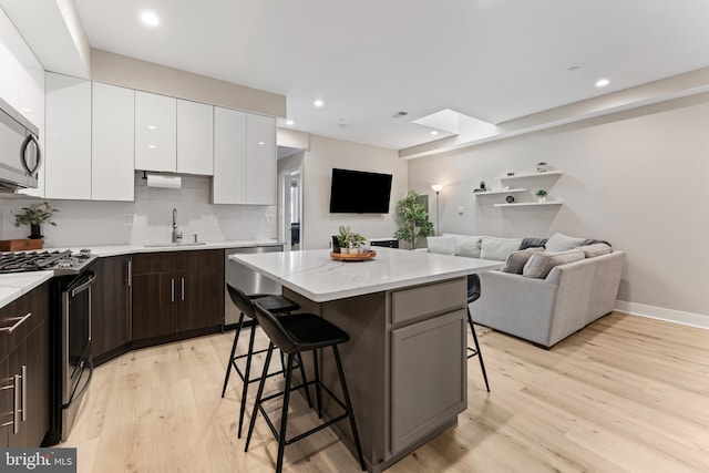 818 Kennedy St NW Unit 9, Washington, DC 20011 - kitchen with appliances with stainless steel finishes, a sink, a breakfast bar, white cabinetry, and light wood-style flooring