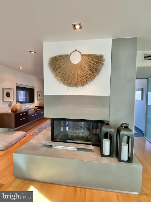 unfurnished living room featuring visible vents, a glass covered fireplace, and wood finished floors