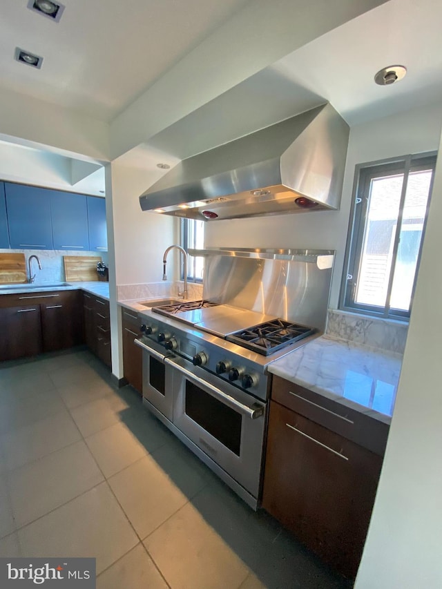 kitchen with dark brown cabinetry, range with two ovens, a sink, light tile patterned floors, and wall chimney exhaust hood