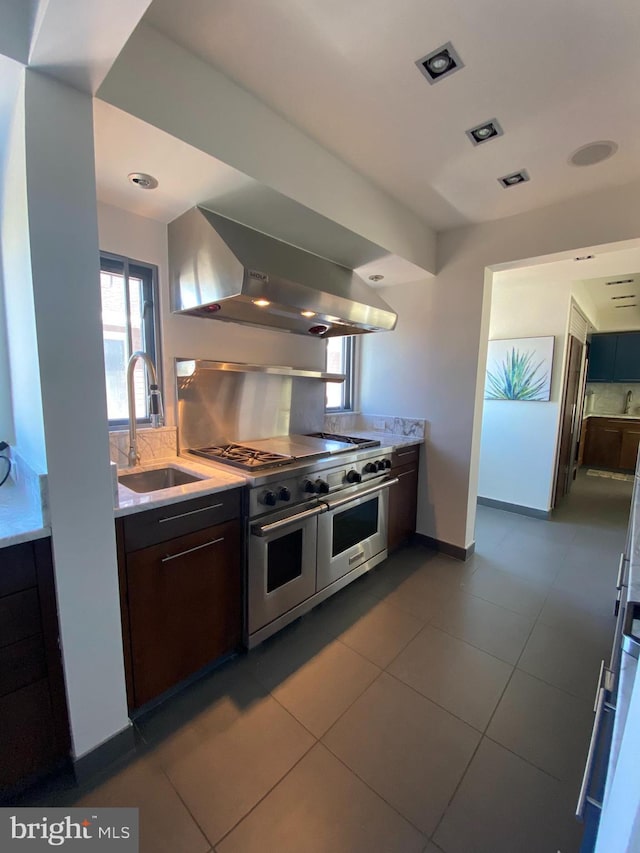 kitchen featuring light countertops, ventilation hood, a sink, backsplash, and double oven range