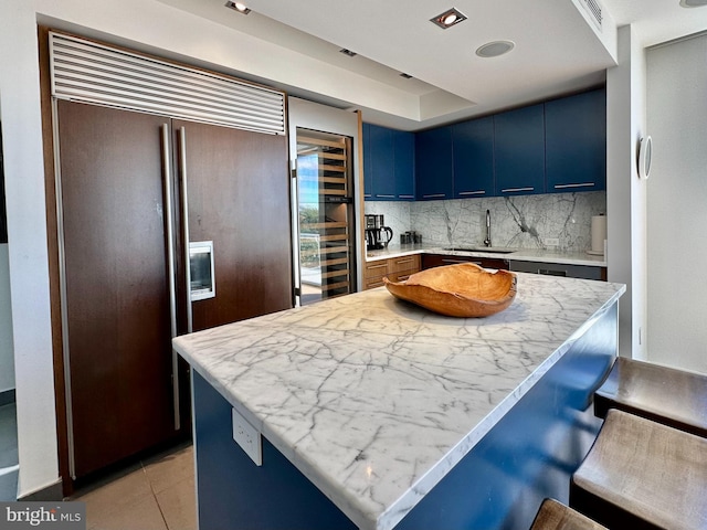 kitchen featuring a breakfast bar, a sink, blue cabinetry, paneled refrigerator, and wine cooler