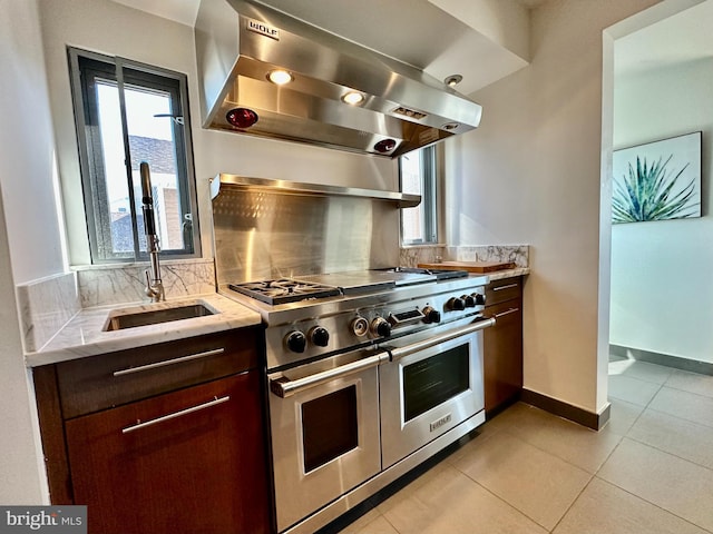 kitchen with exhaust hood, a sink, range with two ovens, light tile patterned floors, and tasteful backsplash