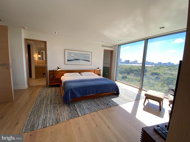 bedroom featuring baseboards, floor to ceiling windows, wood finished floors, and visible vents