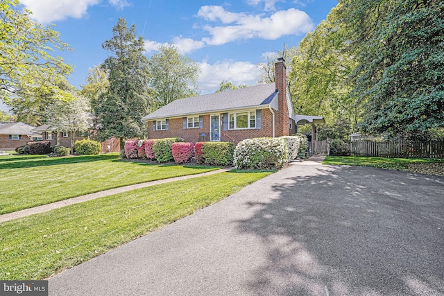 view of front of home featuring driveway, a chimney, a front yard, brick siding, and fence