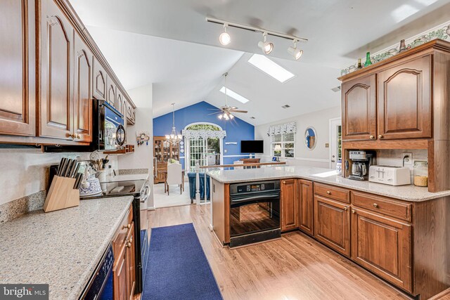kitchen featuring a peninsula, open floor plan, vaulted ceiling with skylight, light wood-style flooring, and black appliances