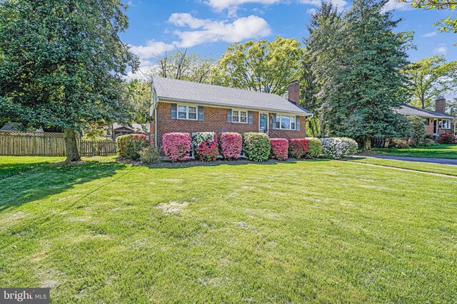 view of front of home featuring brick siding, fence, a chimney, and a front yard