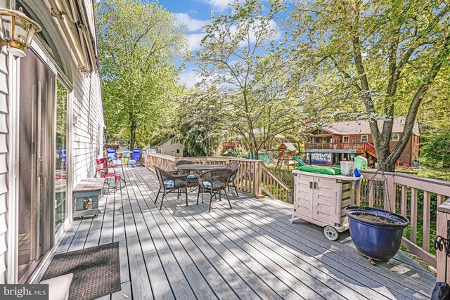 wooden deck with a playground and outdoor dining space