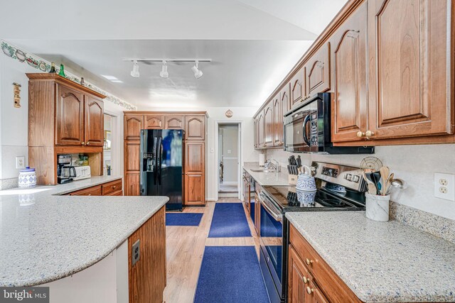 kitchen with brown cabinetry, a peninsula, a sink, light wood finished floors, and black appliances