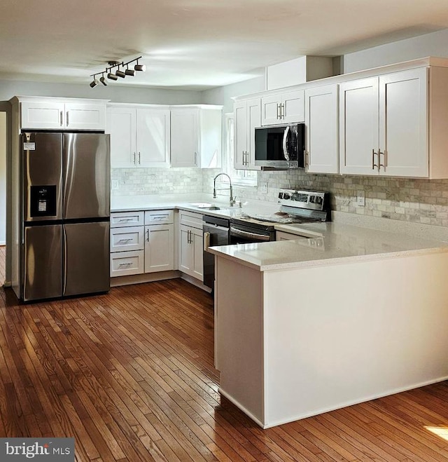 kitchen with a sink, light countertops, stainless steel appliances, a peninsula, and dark wood-style floors