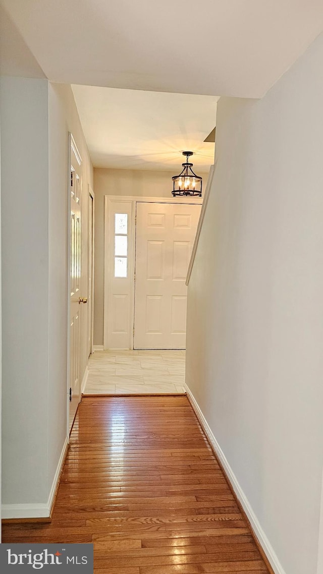 foyer entrance featuring baseboards, a notable chandelier, and light wood-style flooring