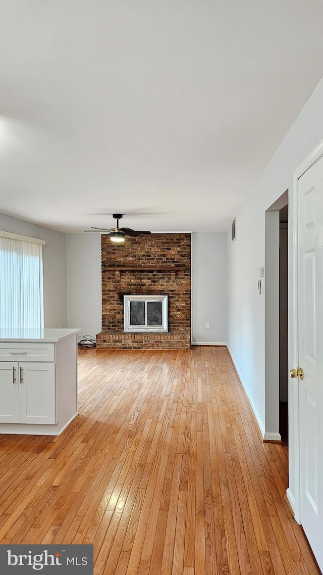 unfurnished living room with ceiling fan, visible vents, a fireplace, light wood-type flooring, and baseboards