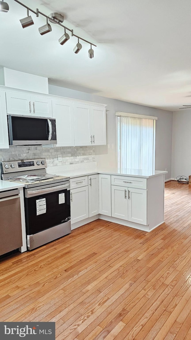 kitchen with decorative backsplash, light countertops, light wood finished floors, stainless steel appliances, and white cabinetry