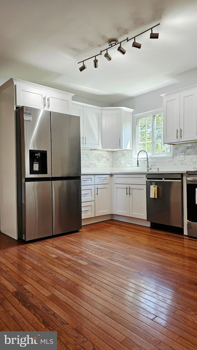 kitchen with decorative backsplash, hardwood / wood-style floors, white cabinetry, a sink, and stainless steel appliances