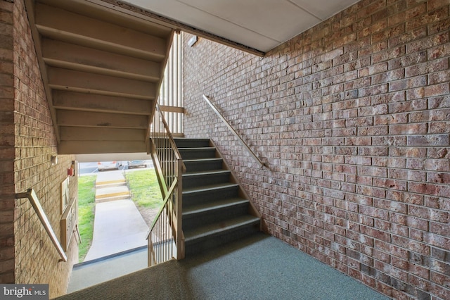 staircase featuring carpet flooring and brick wall