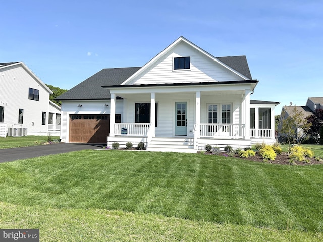 neoclassical / greek revival house featuring aphalt driveway, a garage, a front yard, central air condition unit, and covered porch