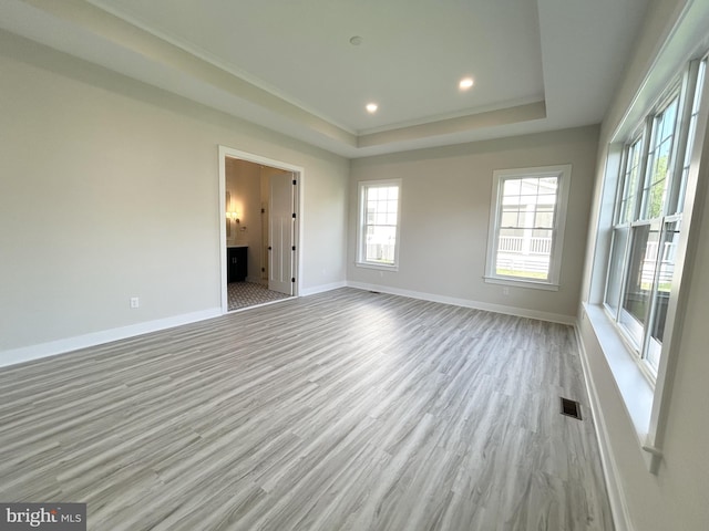 spare room with baseboards, visible vents, wood finished floors, and a raised ceiling