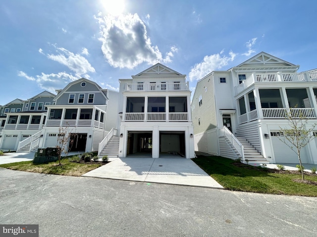 beach home with a garage, a balcony, a sunroom, concrete driveway, and stairway