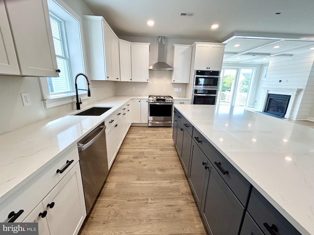 kitchen with wall chimney range hood, a sink, stainless steel appliances, light wood-type flooring, and visible vents