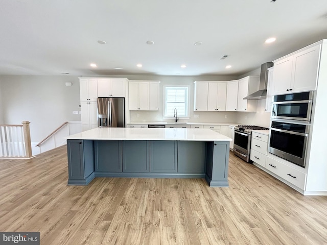 kitchen with appliances with stainless steel finishes, a large island, wall chimney exhaust hood, and white cabinetry