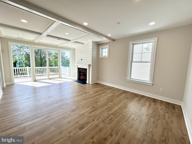 unfurnished living room featuring a healthy amount of sunlight, baseboards, coffered ceiling, and a fireplace with flush hearth