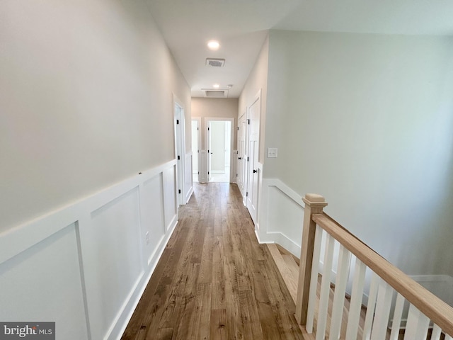 corridor featuring visible vents, wood finished floors, a wainscoted wall, an upstairs landing, and a decorative wall